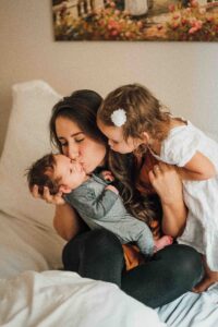 Mother kissing baby with daughter leaning over her